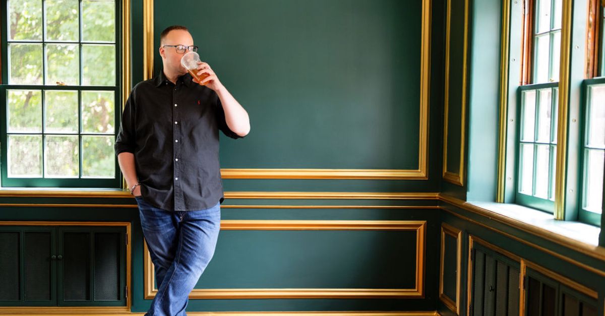 Dr. Mike stands against a green wall, sipping his tea
