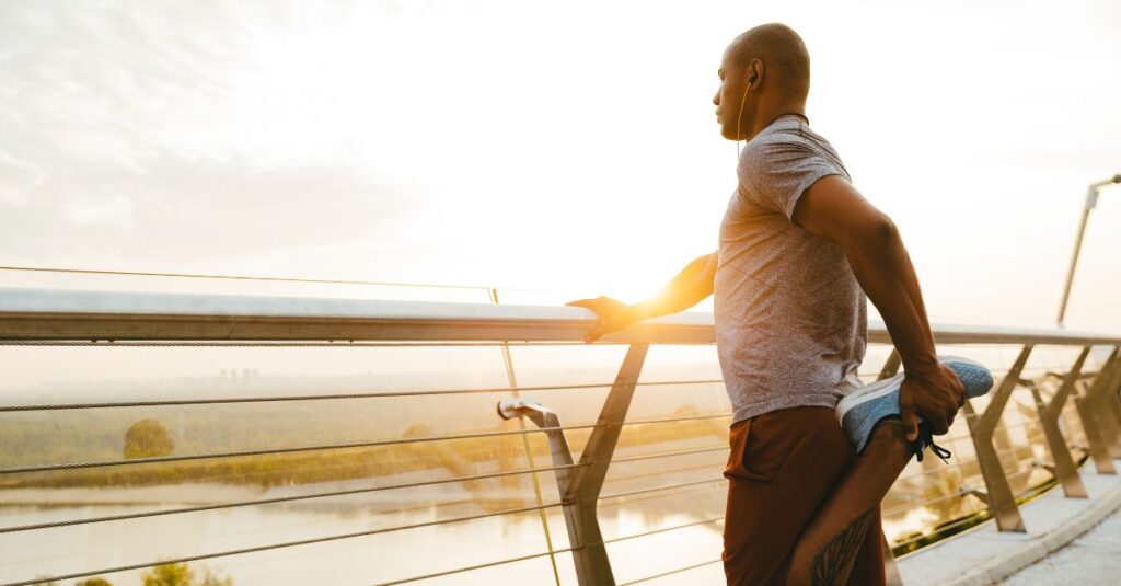 Man warming up for his daily run overlooking a beautiful view from a bridge.