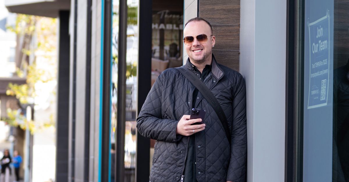 Dr. Mike stands in an urban setting with sunglasses on, smiling brightly at the camera.